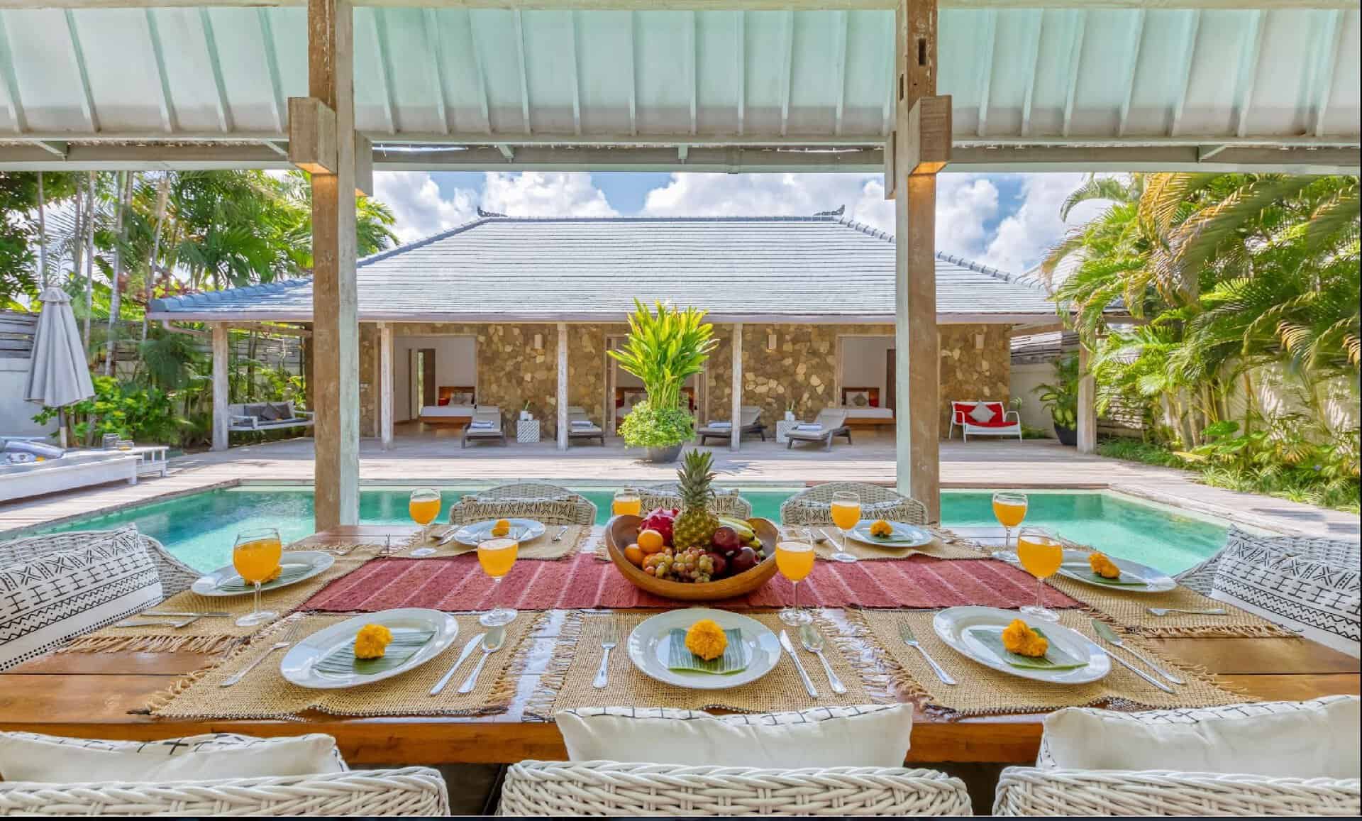 Outdoor dining table beside luxurious pool and villa.