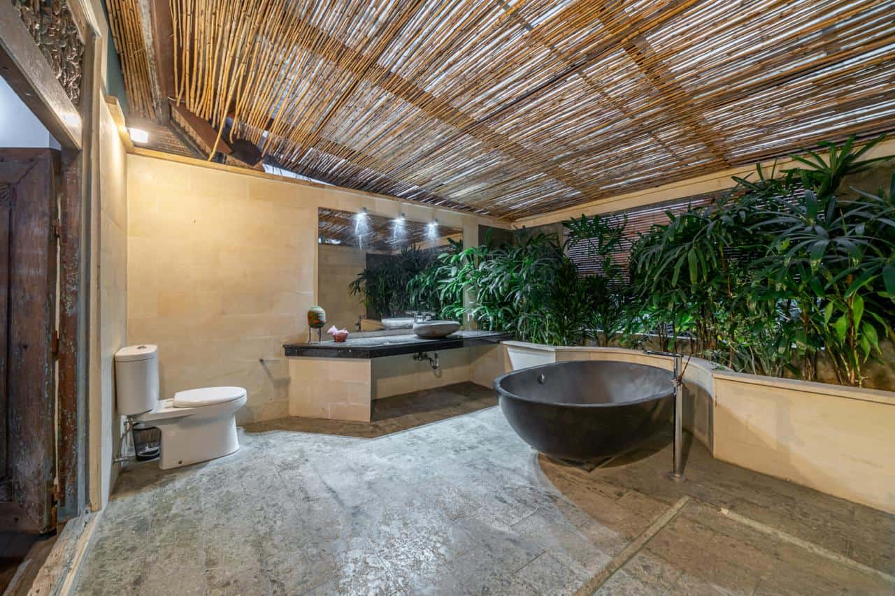 Rustic outdoor bathroom with plants and stone tub.