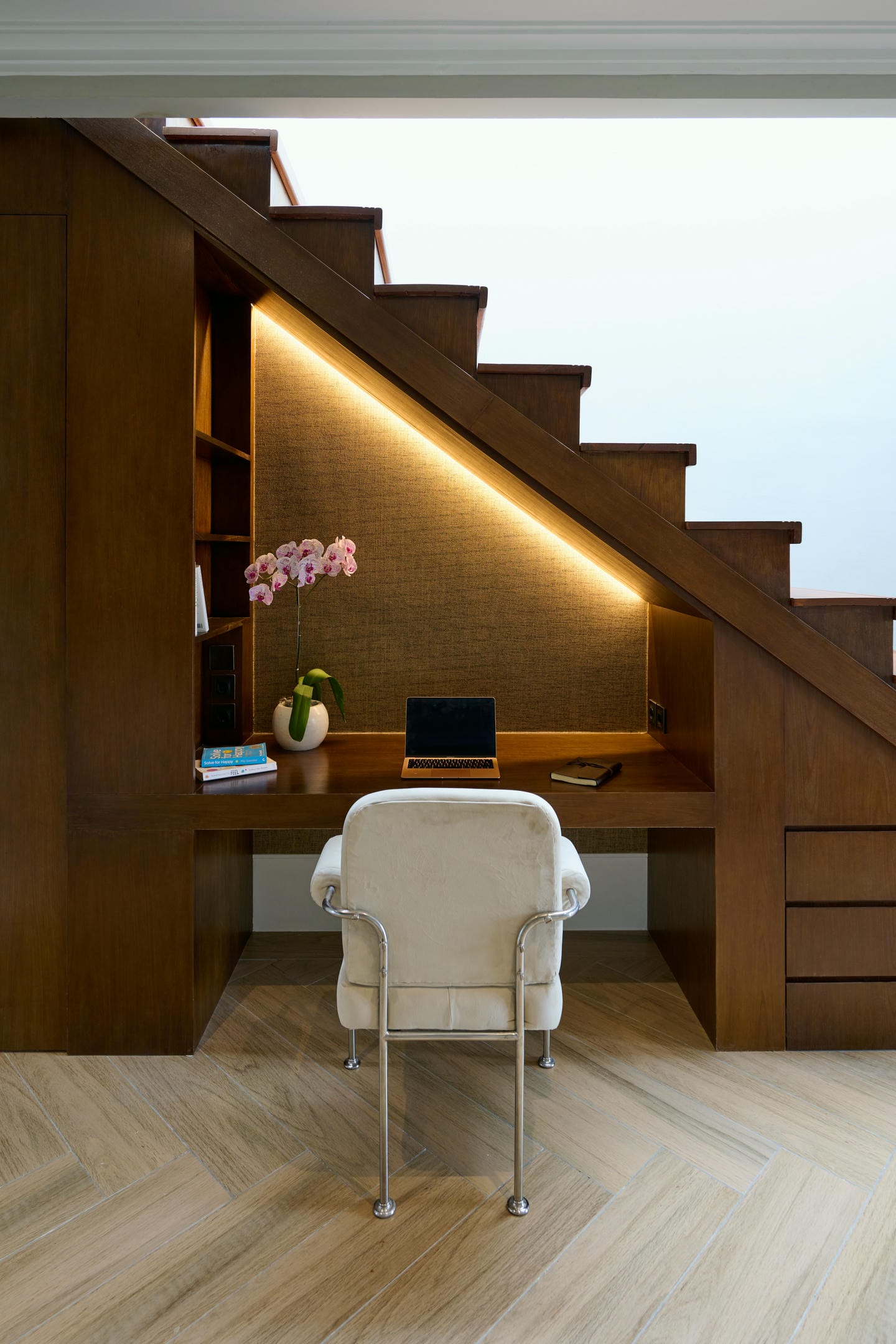 Cozy workspace under staircase with laptop and chair.
