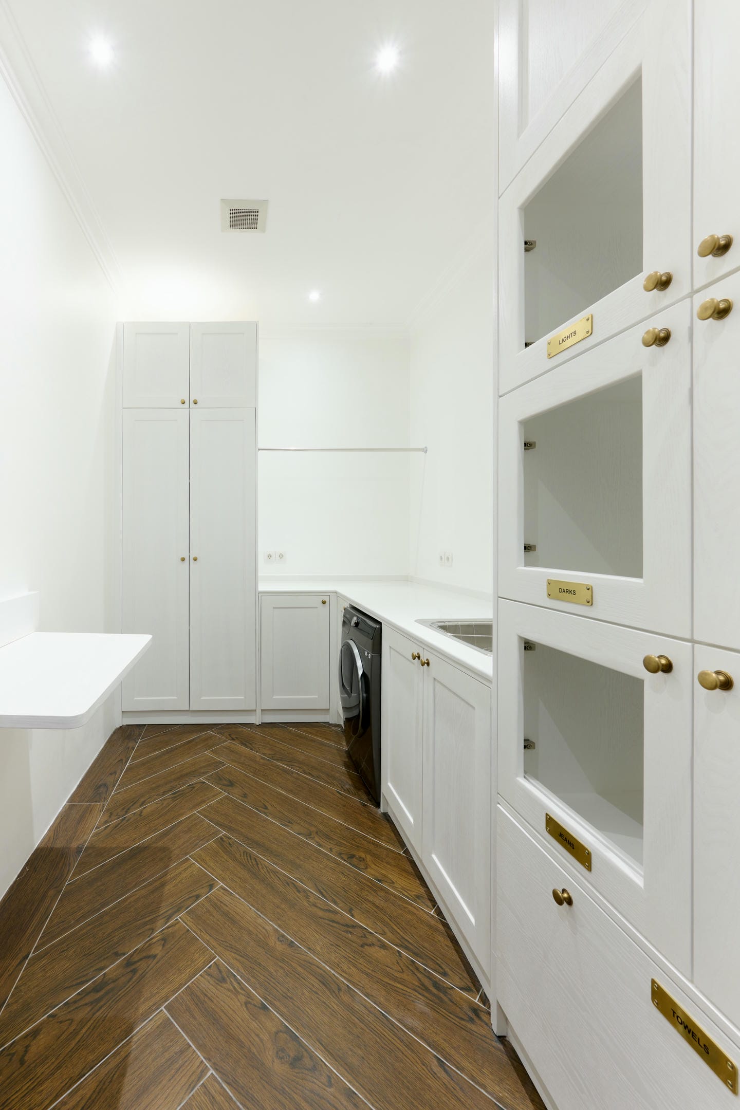 Modern laundry room with wooden floor and white cabinets.