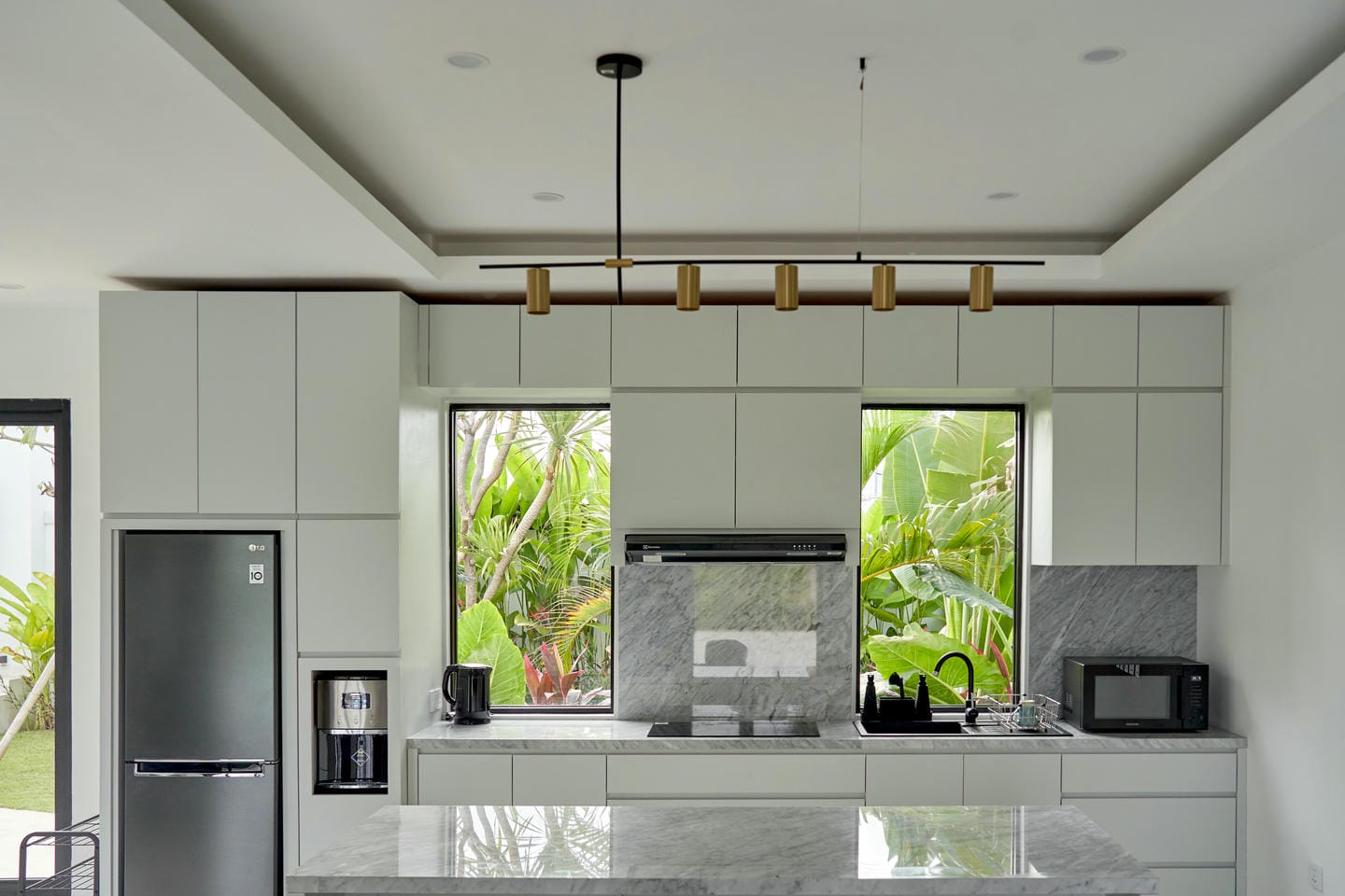 Modern kitchen with marble countertops and greenery view.