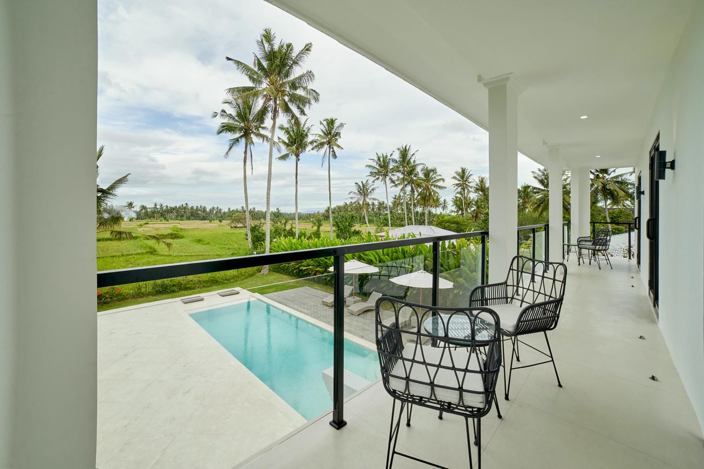 Tropical balcony view with pool and palm trees.