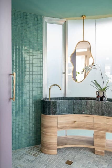Modern bathroom with green tiles and curved sink.