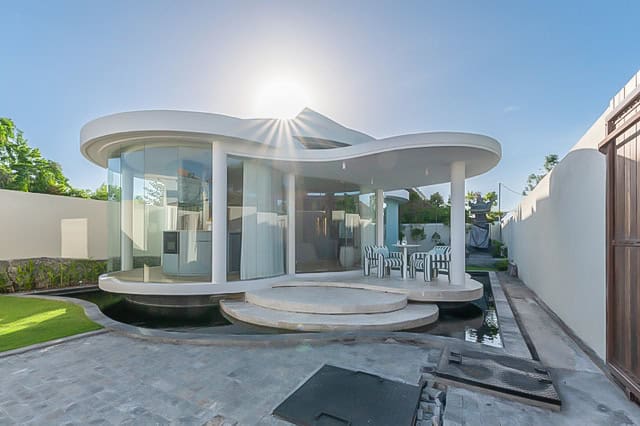 Modern curved glass house exterior with sun overhead.