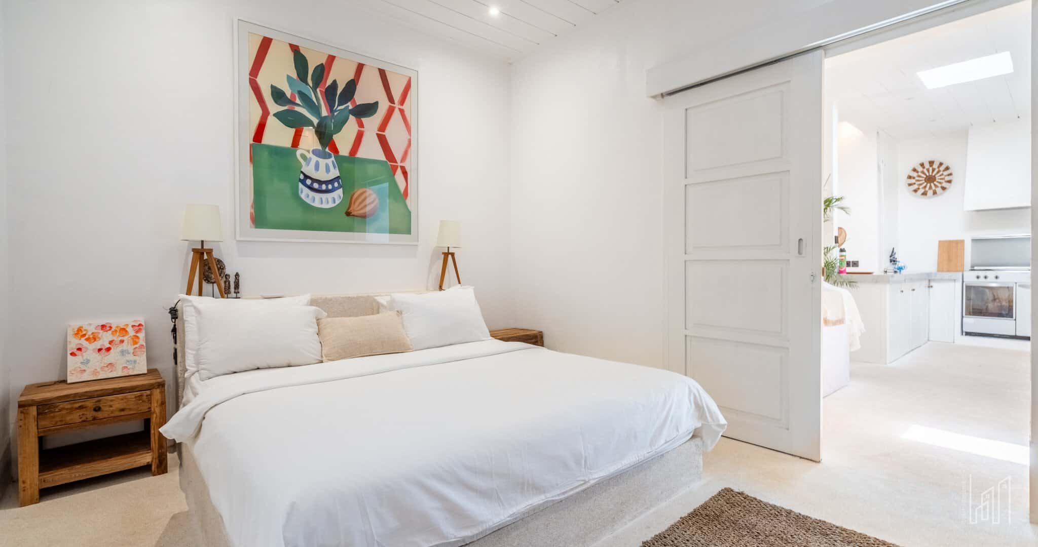 Minimalist white bedroom with cozy decor and painting.