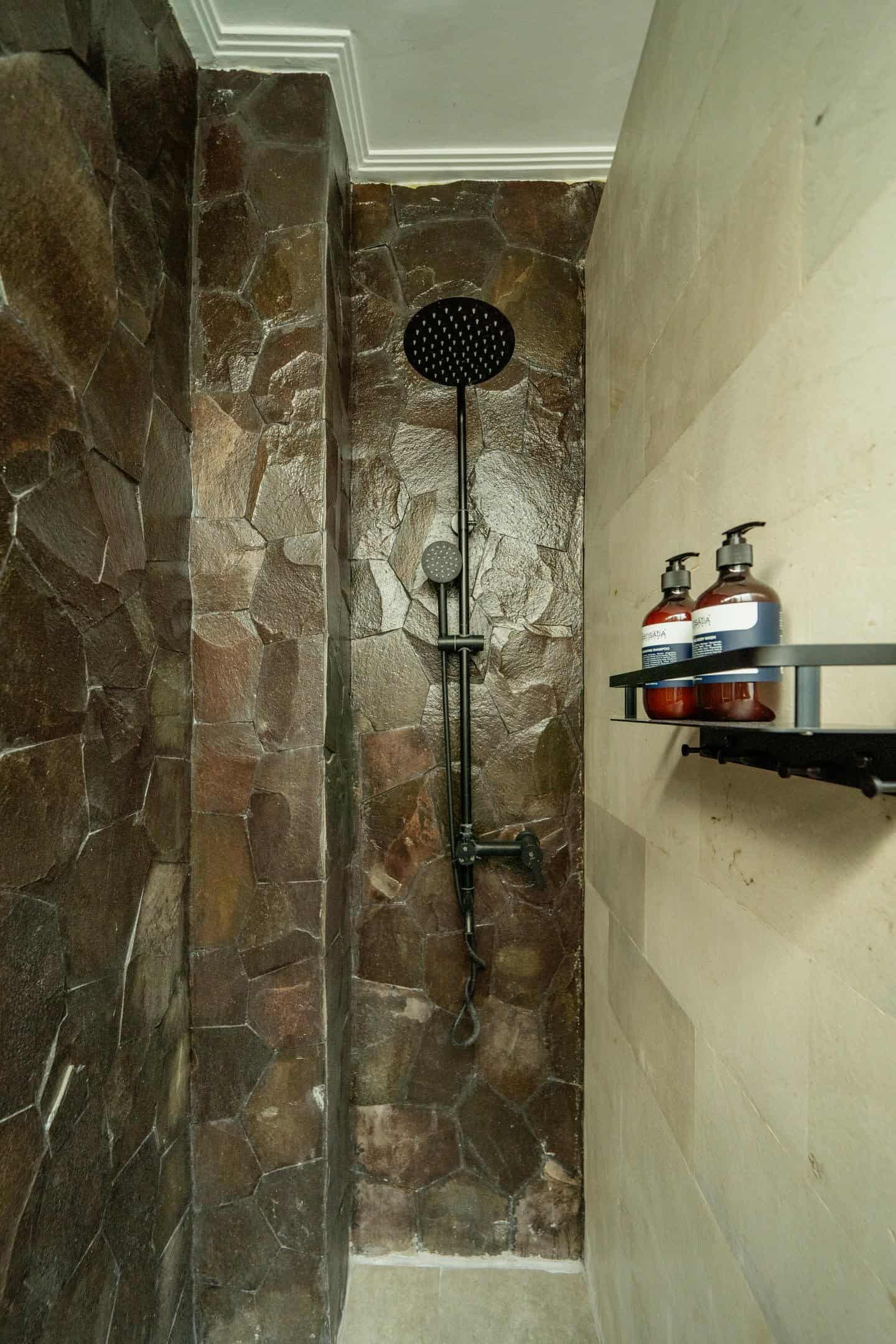 Modern stone shower with dark tiles and toiletries.