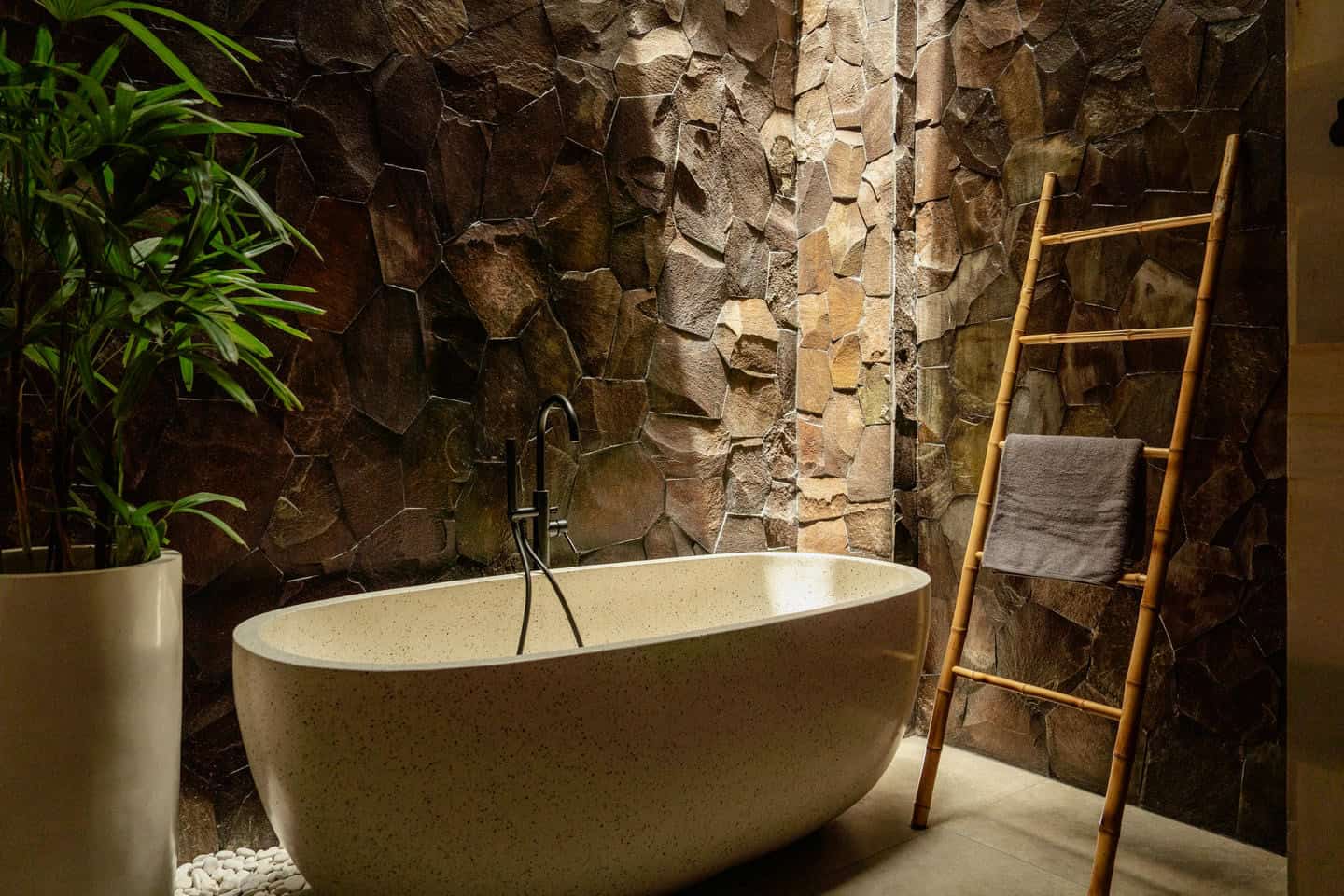 Luxurious stone bathroom with plant and ladder.
