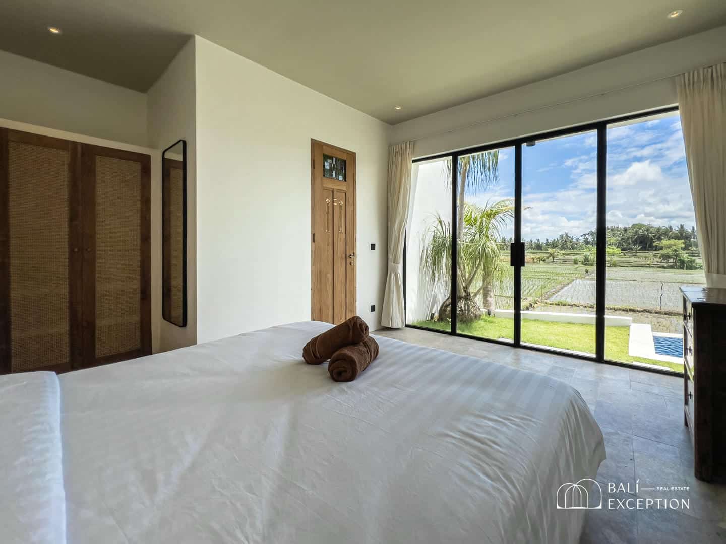 Bedroom with view of rice fields and palm trees.