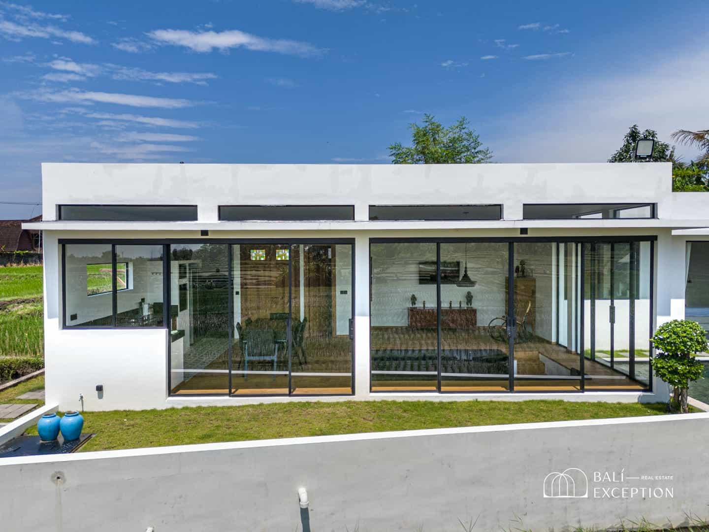 Modern white villa with glass windows in tropical setting.
