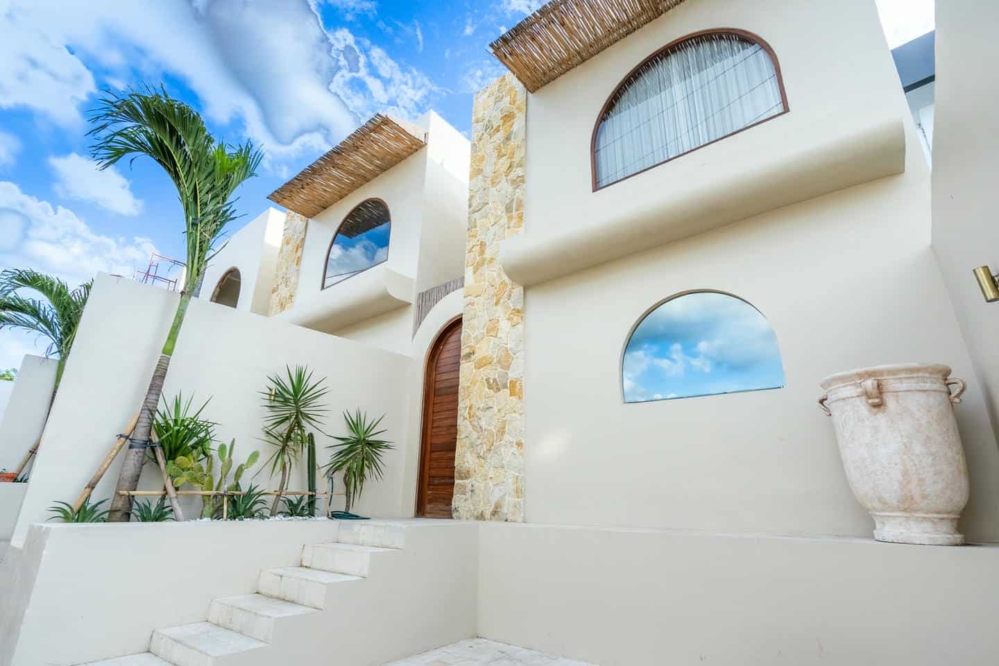 Modern villa exterior with palm trees and blue sky.