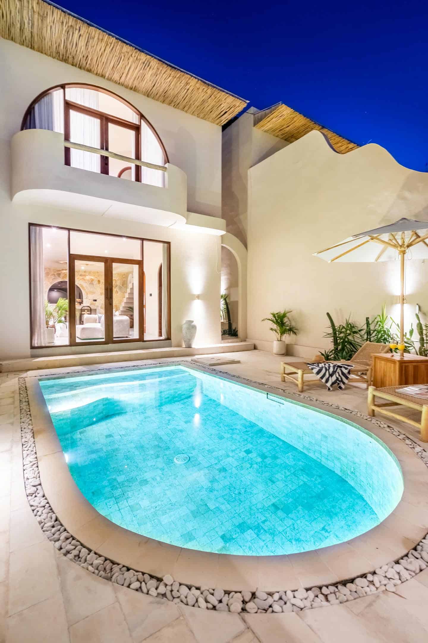 Luxury villa with illuminated pool and patio furniture.