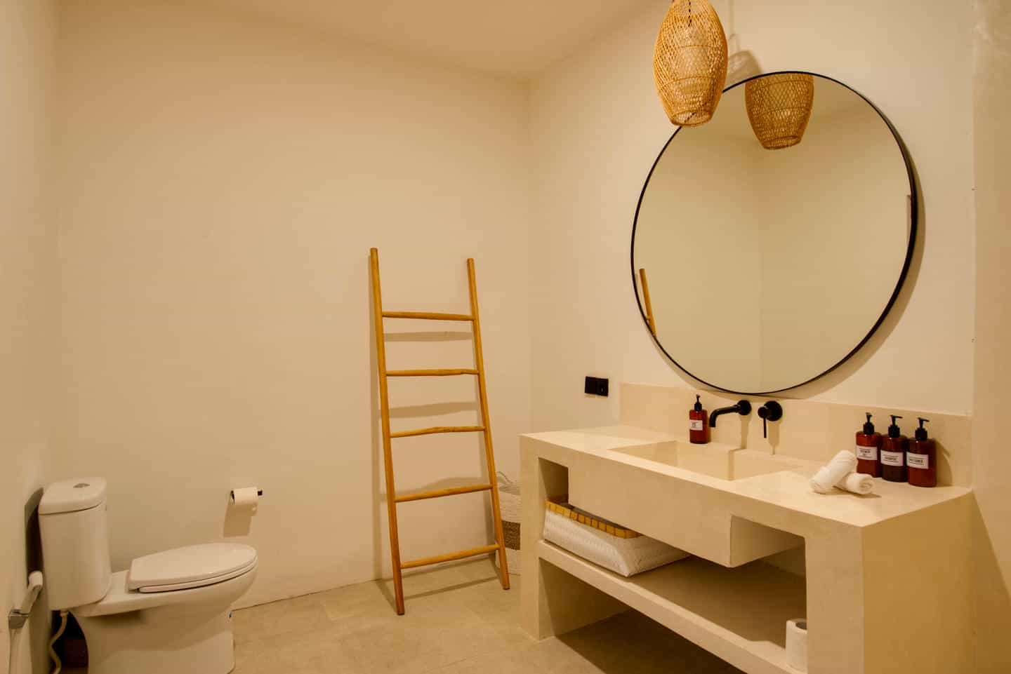 Modern bathroom with round mirror and wooden ladder.