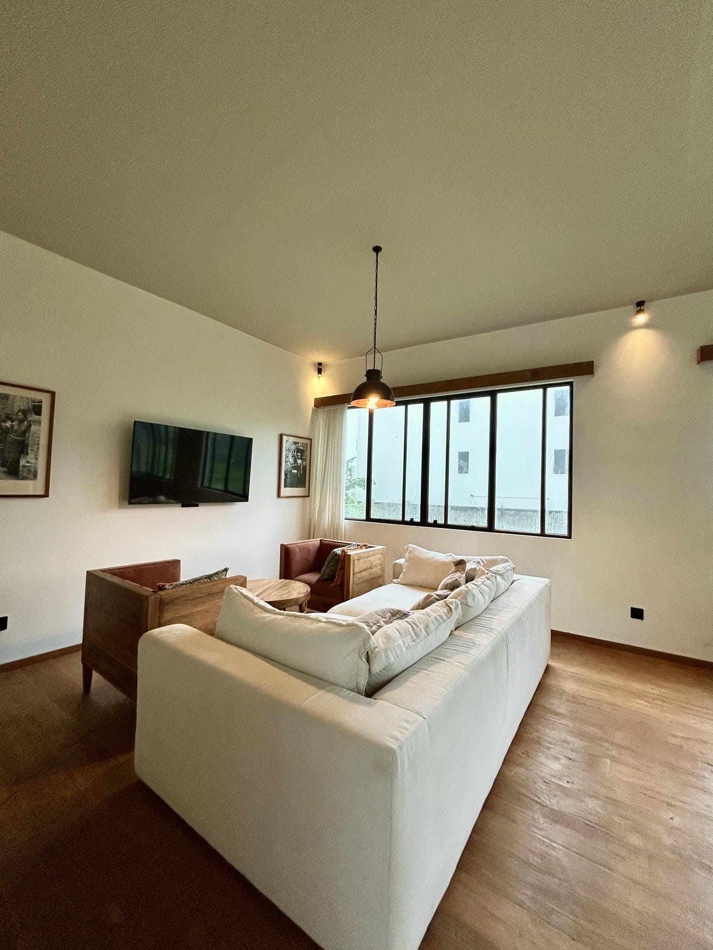 Modern living room with cozy white couch, armchairs, TV.