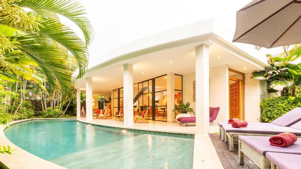 Luxury villa with poolside lounge chairs and greenery.