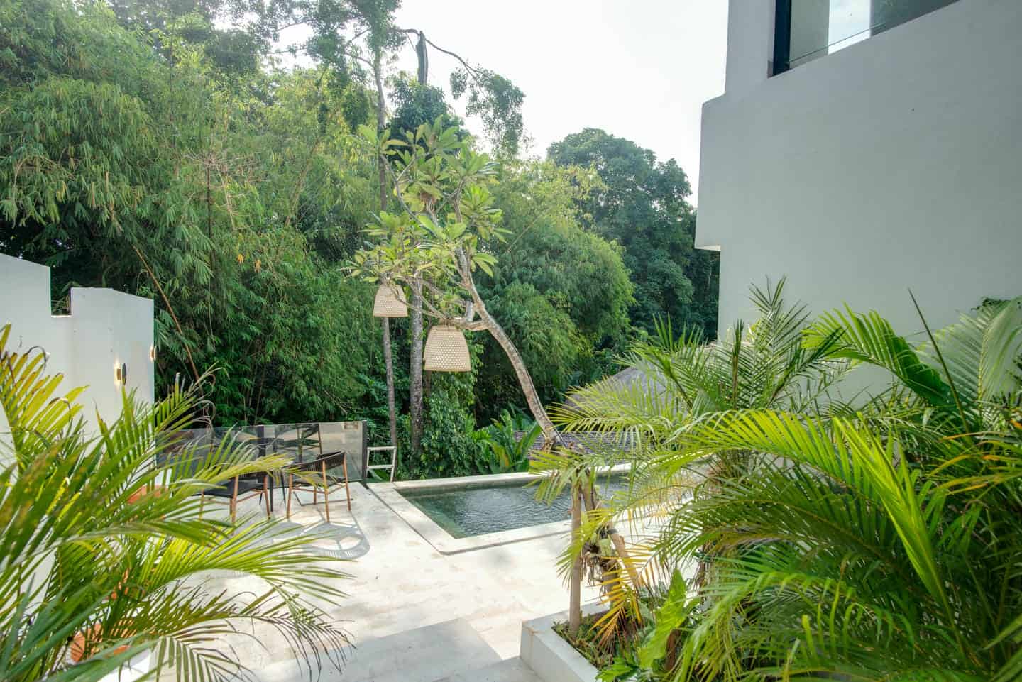 Modern patio with pool and lush greenery backdrop.