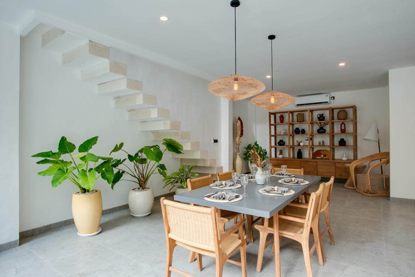 Modern dining area with plants and floating staircase.