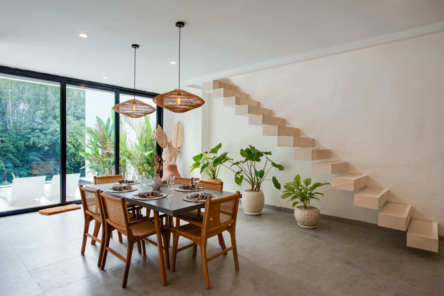 Modern dining room with plants and floating staircase.