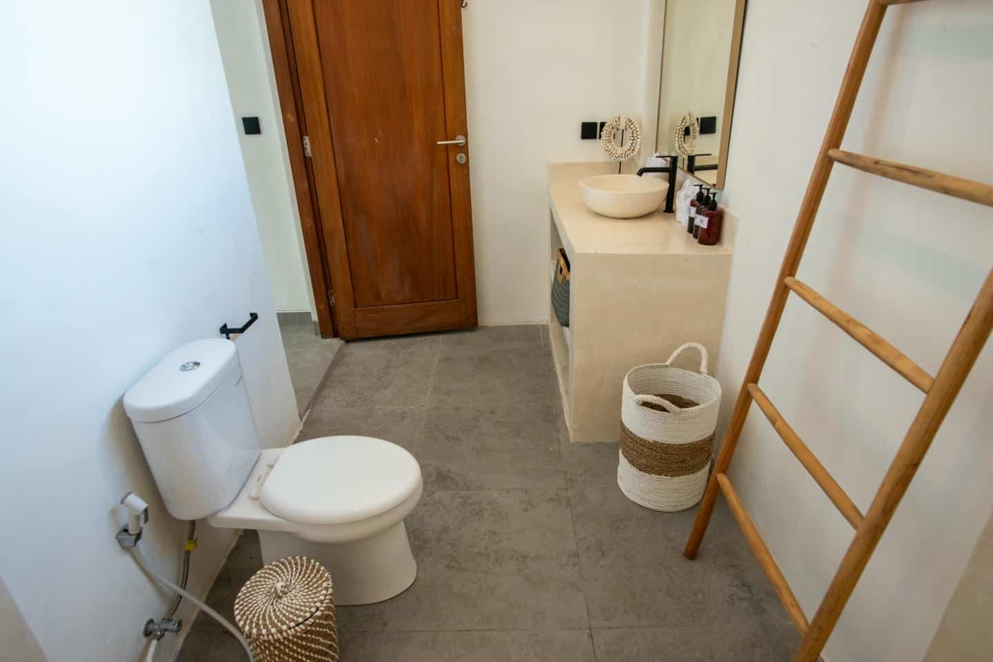 Modern bathroom with toilet, sink, and ladder shelf.