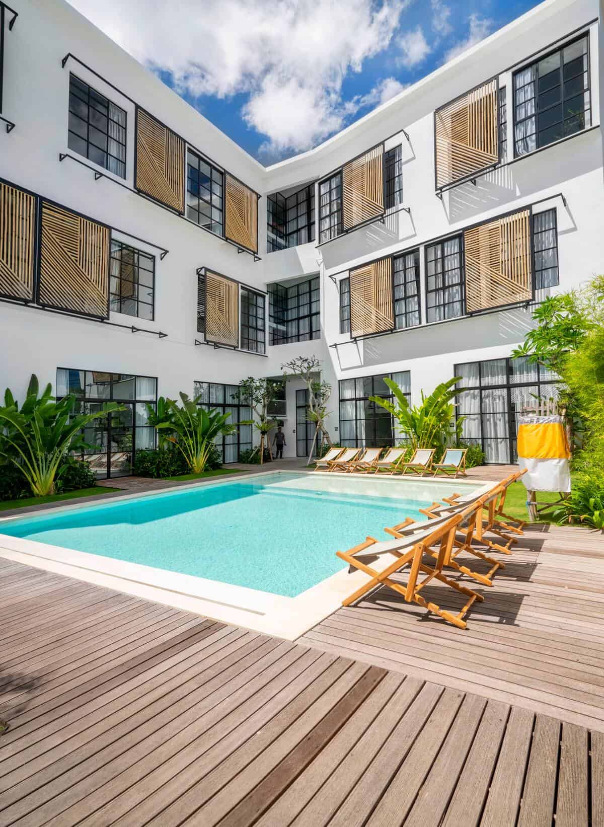 Modern hotel courtyard with pool and deck chairs.