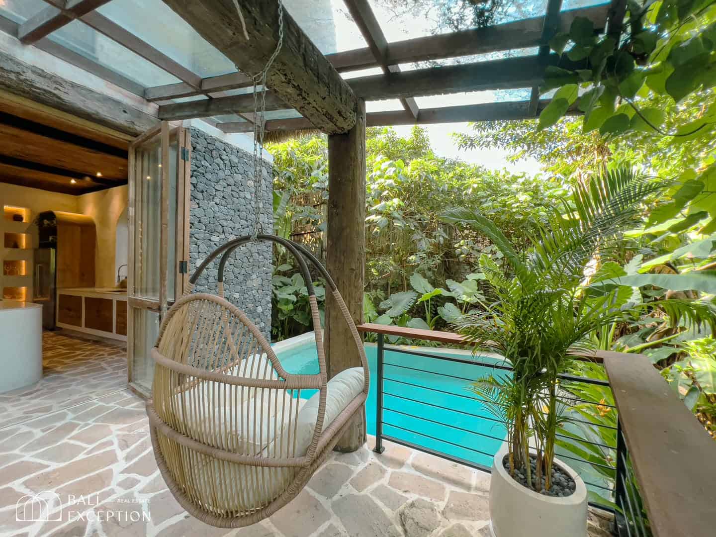 Tropical patio with hanging chair, plants, and pool.