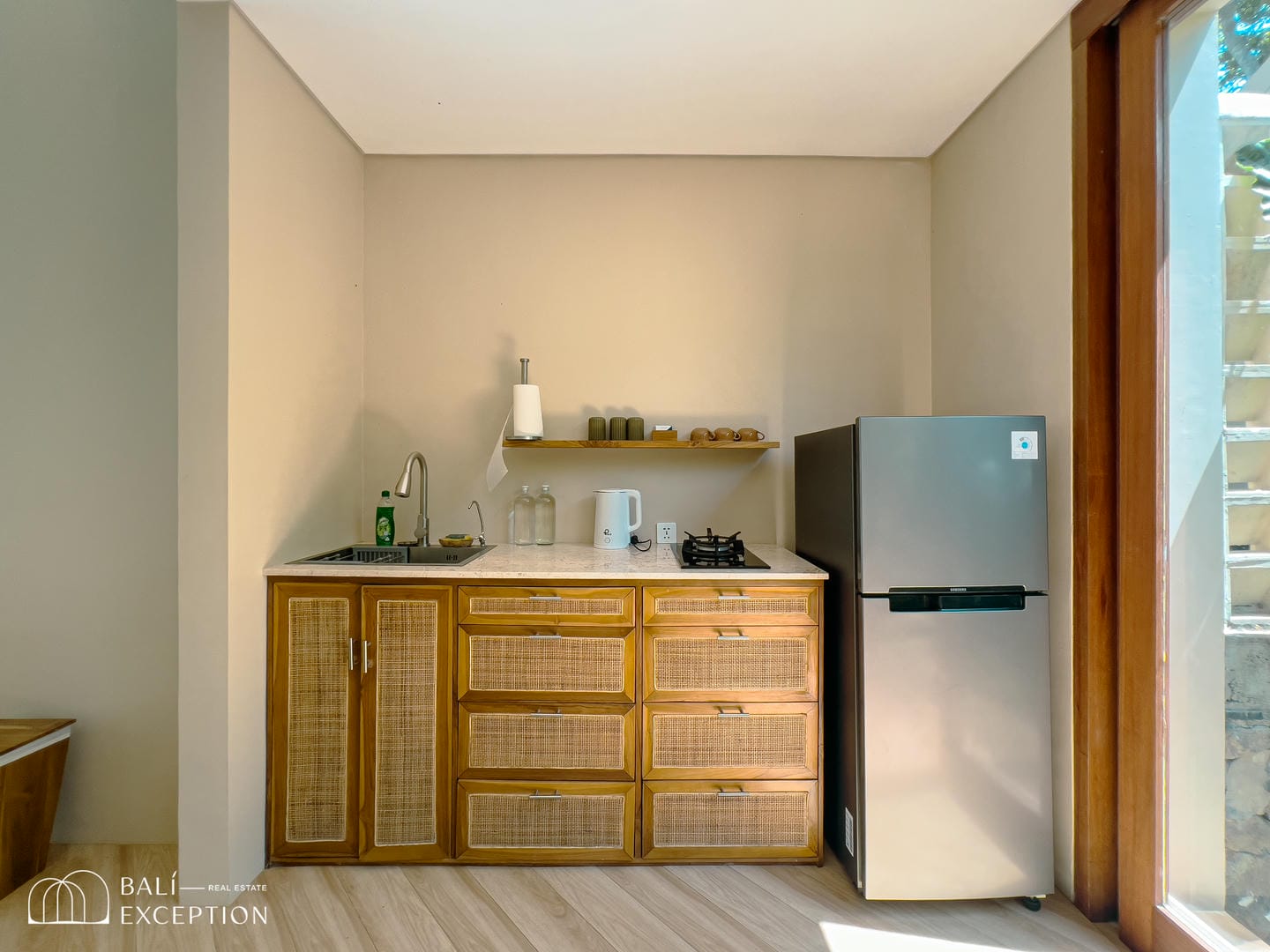 Modern kitchenette with wooden cabinets and silver fridge.